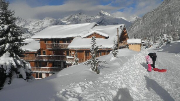 Un albergue en la montaña cubierto de nieve, con varios balcones y un telesilla al fondo.