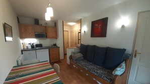 Una habitación compacta con cama, sofá, mesa de comedor y kitchenette.