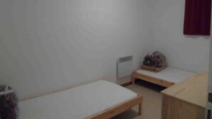 A small, sparsely furnished room with two single beds, a wooden bench, and a radiator. - Ground floor, view valley, tv, ski locker, 31m², Valfréjus (Valfréjus)