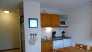 A compact kitchen with wooden cabinets, a microwave, and a coffee maker. There is a dining table with chairs. - Ground floor, view valley, tv, ski locker, 31m², Valfréjus (Valfréjus)