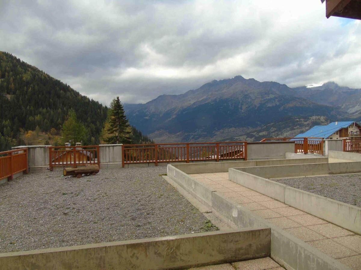 A rooftop terrace with a gravel floor, a wooden fence, and a view of mountains.