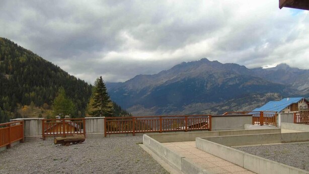 A rooftop terrace with a gravel floor, a wooden fence, and a view of mountains.