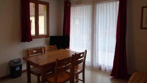 A dining area with a wooden table and chairs, a television, and a window with curtains. - Ground floor, view valley, tv, ski locker, 31m², Valfréjus (Valfréjus)