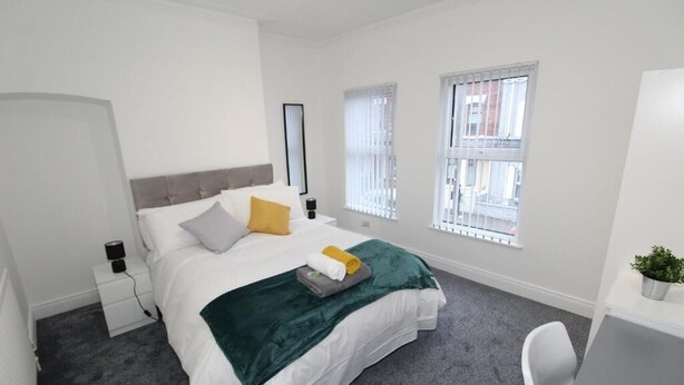 A modern bedroom with a bed, bedside tables, a desk, and a window.