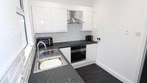 A compact kitchen with white cabinets, a stainless steel range hood, a black countertop, and a sink.