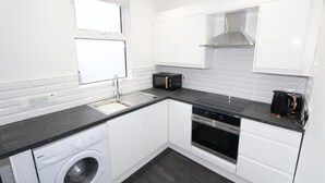 A modern kitchen with white cabinets, a built-in oven, a dishwasher, and a coffee maker.