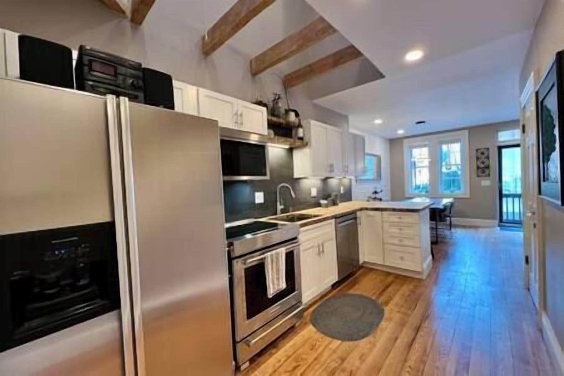 A modern kitchen with stainless steel appliances, wooden beams, and a large window.