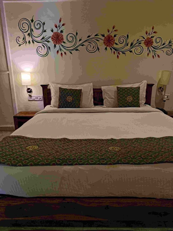 A bedroom with a large bed, two decorative pillows, a nightstand, and a wall-mounted lamp. - The Hotel Rajputana (Sawai Madhopur)
