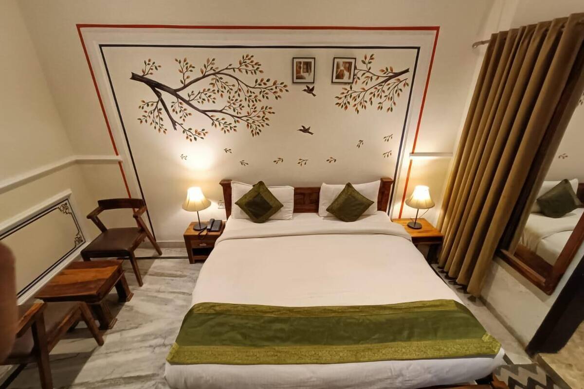 A neatly arranged hotel room with a large bed, two bedside tables with lamps, a headboard with a tree mural, and a mirror on the wall.