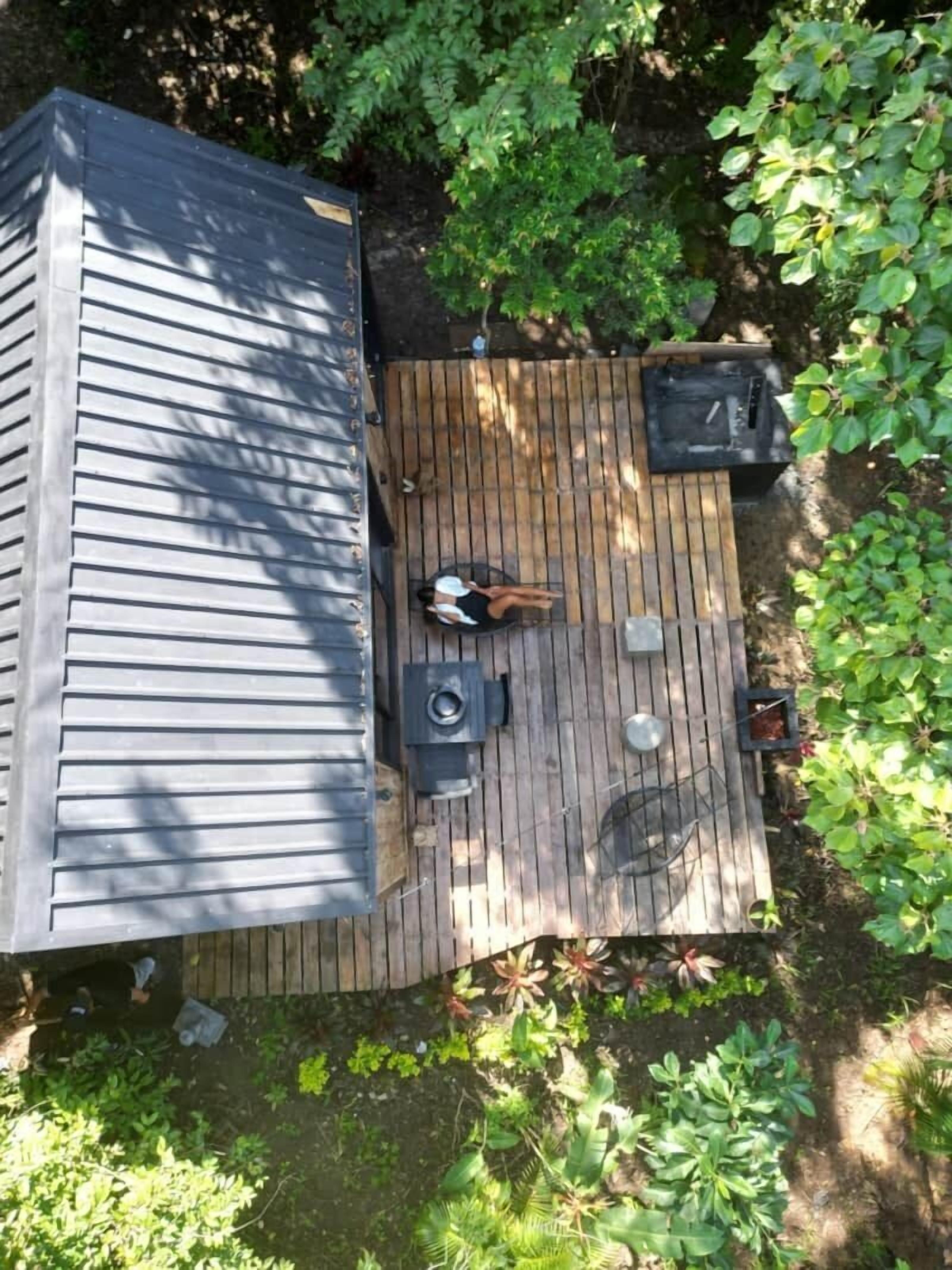 Una terraza de madera con zona de estar cubierta, una parrilla y un cobertizo pequeño.