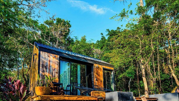 A wooden cabin with a balcony, surrounded by dense forest. - Kooteja Anton Valley ËRA (Los Llanitos)
