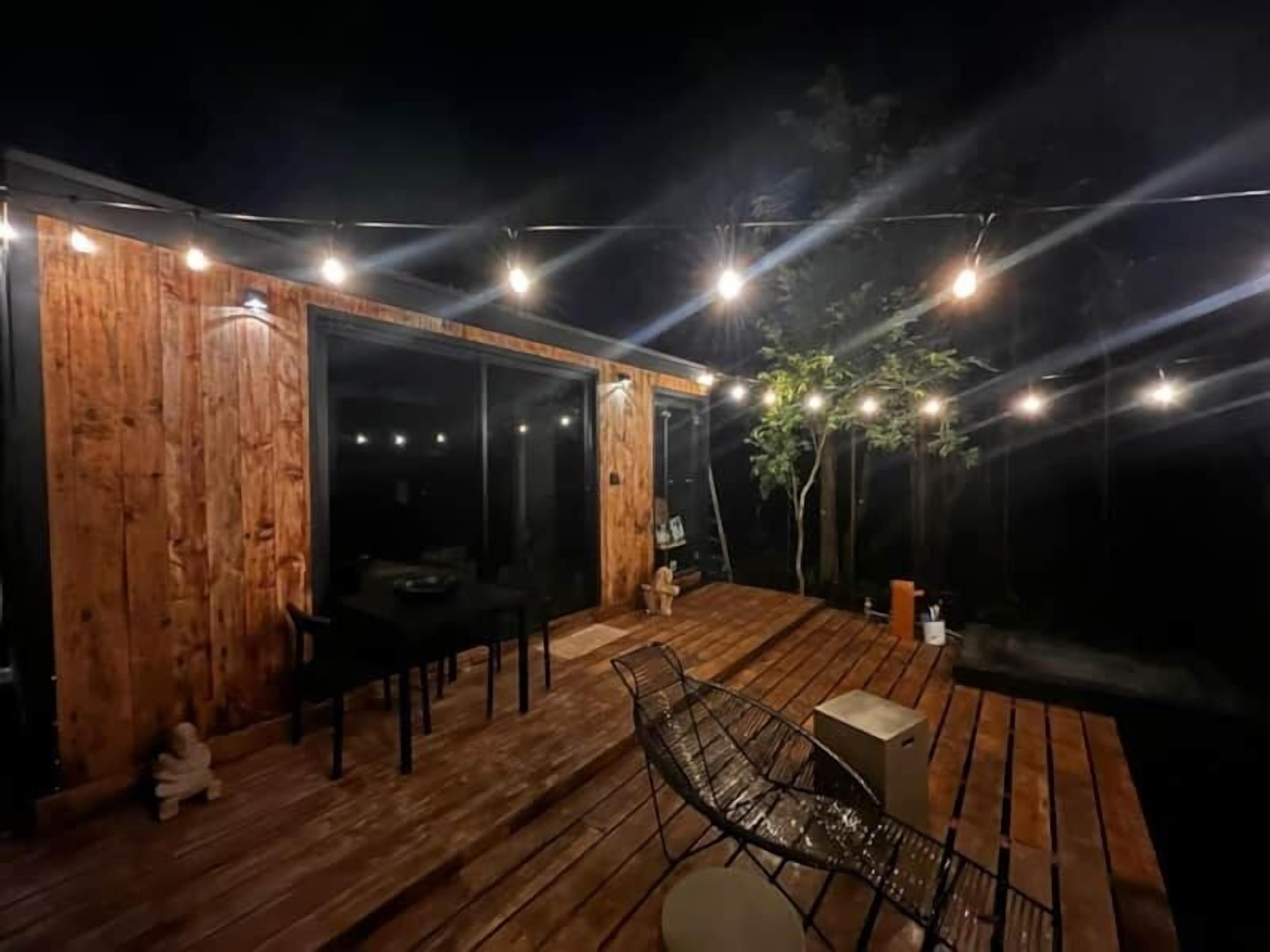 Une terrasse extérieure en bois, dotée d’un espace repas comprenant une table et des chaises, ainsi que d’un petit coin salon avec un banc.