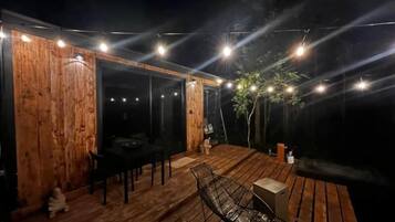 Une terrasse extérieure en bois, dotée d’un espace repas comprenant une table et des chaises, ainsi que d’un petit coin salon avec un banc.