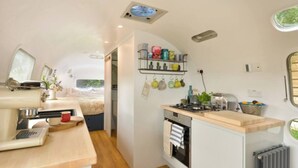 Una cocina compacta con estufa, lavamanos y una pequeña encimera. Se ve una cama al fondo, lo que sugiere una kitchenette.