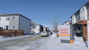 A residential street with snow-covered ground, a white car parked on the side, and a sign for 'ASCENT condos FAIRFIELD PARK'.