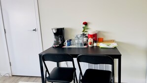 A small kitchenette with a coffee maker, water bottles, a red rose, and baby wipes on the counter.