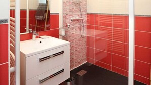 Et badeværelse med et hvidt toiletbord, en brusekabine i glas og vægge med røde og beige fliser.