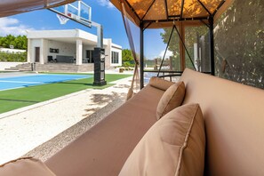 Un'area salotto esterna coperta con piscina, un edificio moderno sullo sfondo e cielo sereno.