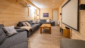 Acogedor interior de cabaña de madera con un conjunto de sofás, una mesa de centro y una pantalla grande para ver contenido.