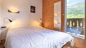 Un dormitorio con cama, lámparas de noche, una pared de madera y un ventanal con vistas a un paisaje boscoso.