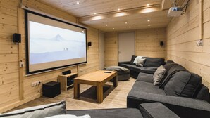 Una habitación acogedora con una pantalla grande, paredes de madera, un sofá y una mesita.