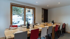 Comedor con mesa de madera dispuesta para seis personas, sillas alrededor y vistas a un paisaje nevado a través de amplios ventanales.