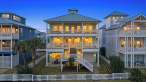 A multi-story beachfront property with balconies, a covered outdoor seating area, and a staircase leading to the upper floors.