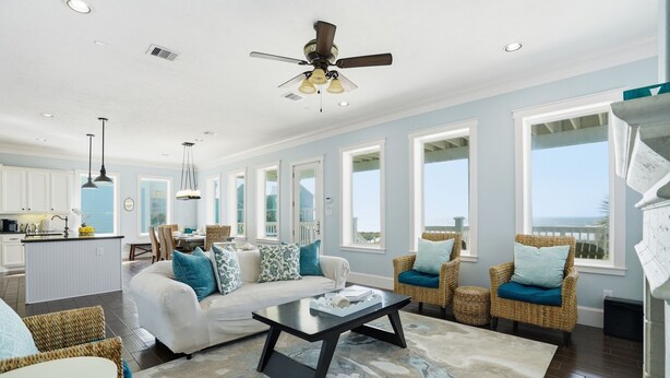 A spacious living area with a sofa, coffee table, wicker chairs, and large windows offering a view.
