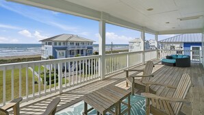 A wooden deck with a view of the ocean, a white railing, and a blue house in the background.