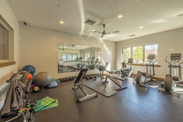 Un gimnasio con equipamiento de ejercicio, un espejo y ventanas que dejan entrar luz natural.