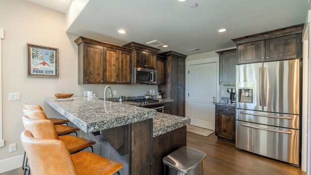 Una cocina moderna con armarios de madera oscura, electrodomésticos de acero inoxidable, encimera de granito y una zona de asientos tipo barra.