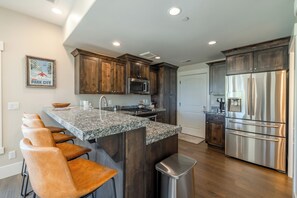 A modern kitchen with dark wood cabinets, stainless steel appliances, a granite countertop, and a bar seating area.