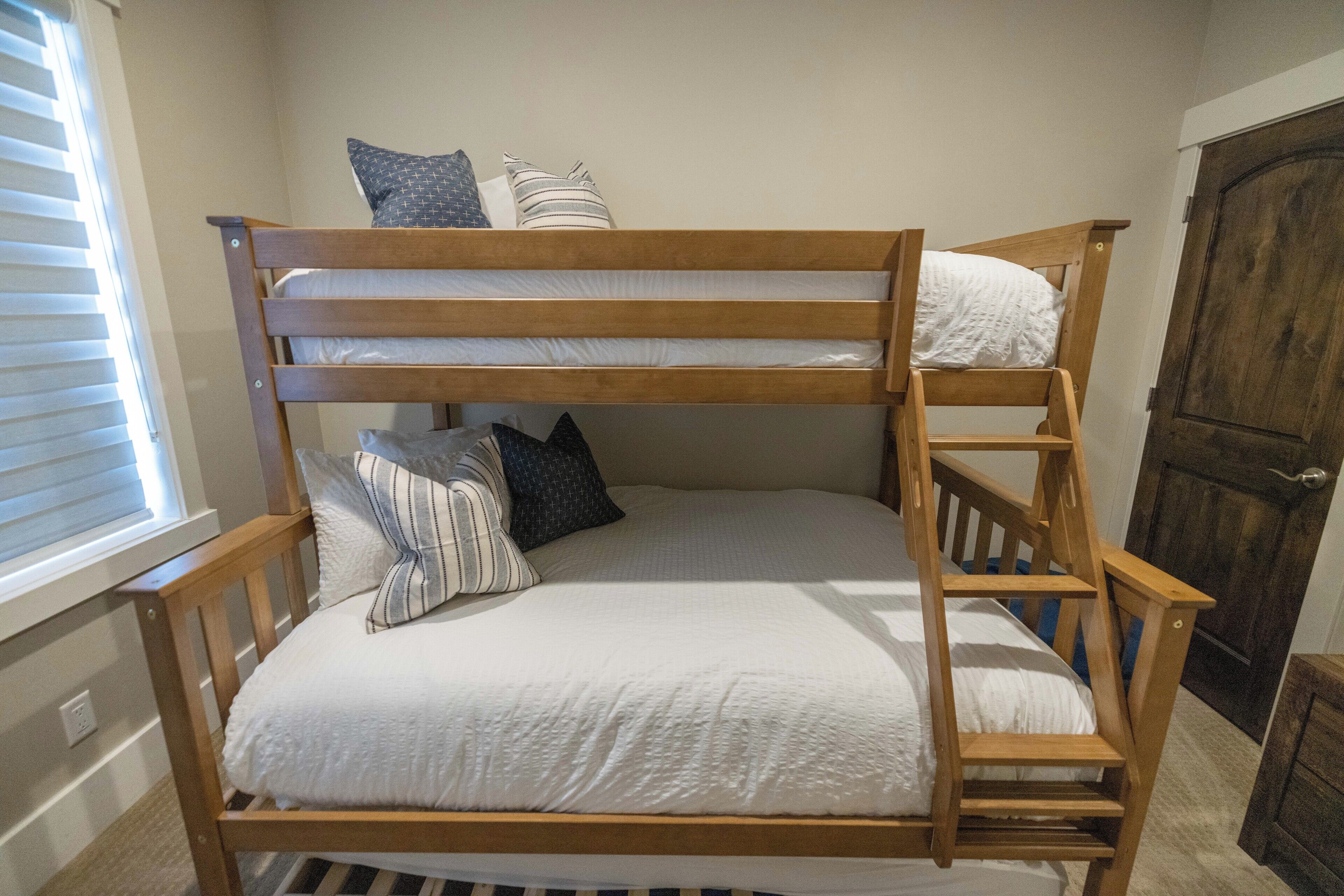 A bunk bed with a wooden frame, white bedding, and striped pillows.