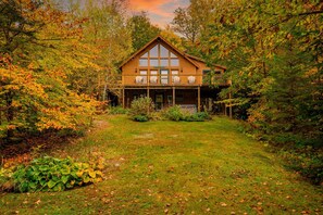 A wooden cabin with a balcony, surrounded by autumn foliage. - Private dog-friendly lodge with hot tub, mountain views, and fenced-in yard (Bethel)