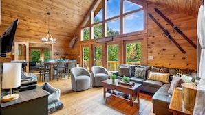 Un intérieur de cabine spacieux, avec un plafond haut, des murs en bois, un coin repas et un salon confortable doté d’un canapé et de fauteuils.