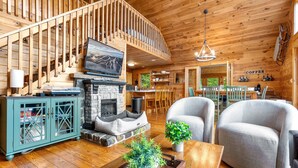 L’intérieur d’un chalet en bois comprend une cheminée, un coin repas et un salon avec un téléviseur et des sièges.