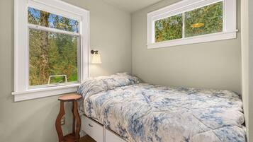 A bedroom with a single bed, two windows, a bedside table, and a lamp.