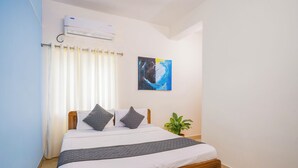 A bedroom with a bed, curtains, a wall-mounted air conditioner, a painting, and a potted plant.
