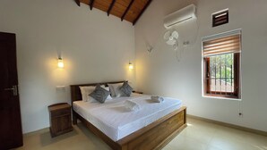 Une chambre avec un lit en bois, deux tables de chevet, un climatiseur, une fenêtre avec des stores et un ventilateur fixé au mur.
