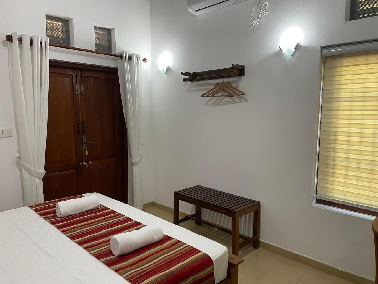A bedroom with a bed, a small table, a wardrobe, and a window with blinds.