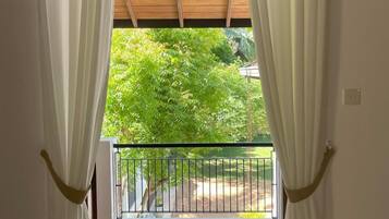 Una habitación con un ventanal grande, cortinas blancas, techo de madera y un balcón con barandilla de metal.