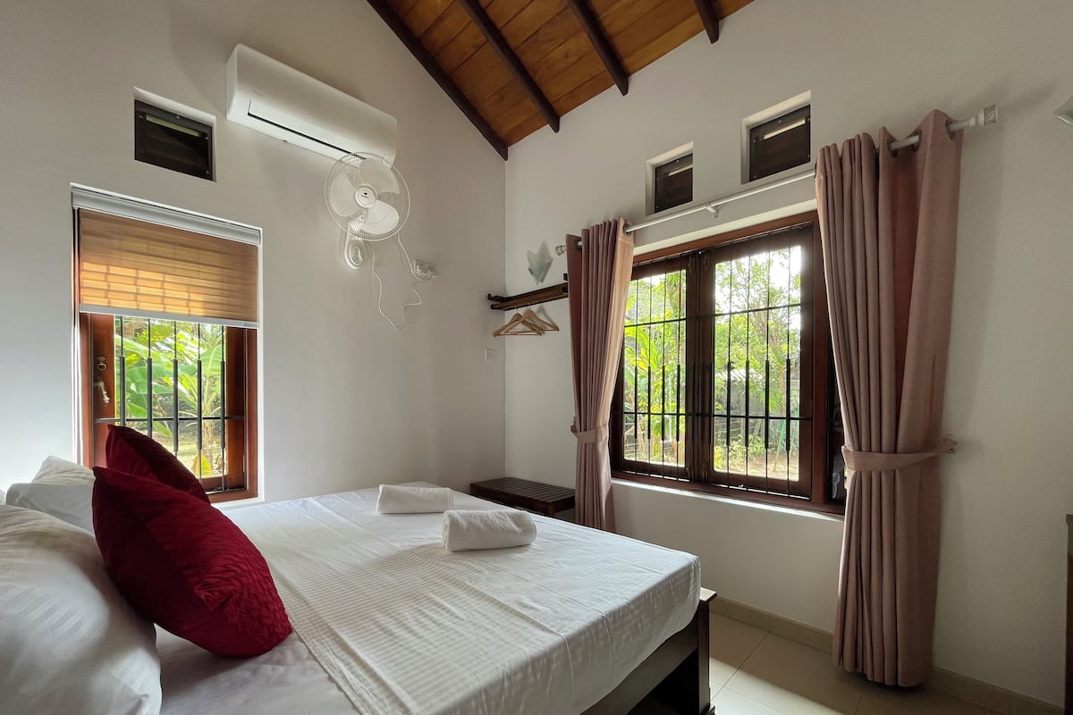 A bedroom with a bed, a window with curtains, an air conditioning unit, and a ceiling fan.