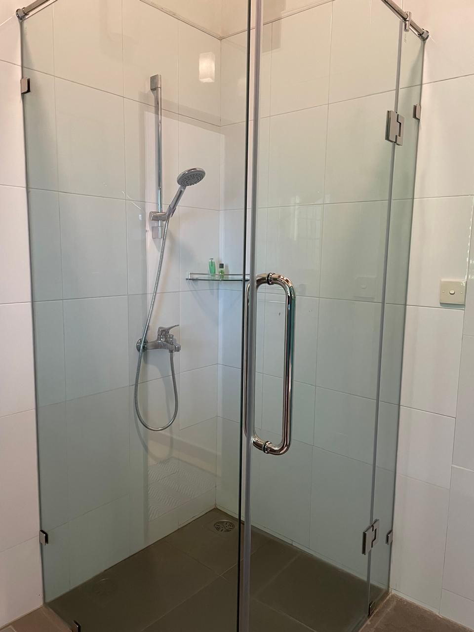 A glass-enclosed shower with a handheld showerhead and a wall-mounted faucet.