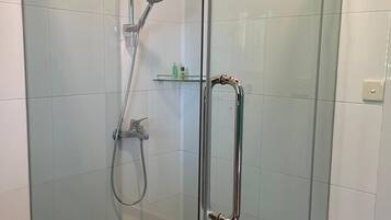 A glass-enclosed shower with a handheld showerhead and a wall-mounted faucet.