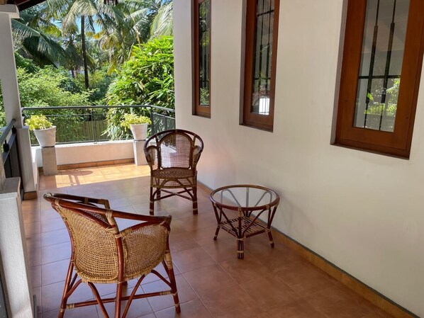 A balcony with wicker furniture, a glass table, and a view of lush greenery. - Cenreeza Airport Villa (Negombo)