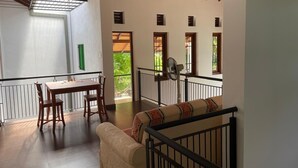 Une pièce spacieuse avec un plafond en bois, une table à manger avec des chaises, un canapé et un balcon offrant une vue sur la verdure.