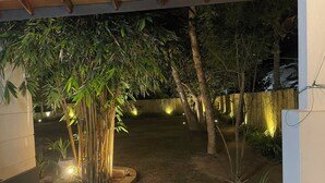 Un espace extérieur aménagé pour la nuit, avec des plantes en bambou, un jardinière circulaire et une clôture en bois.