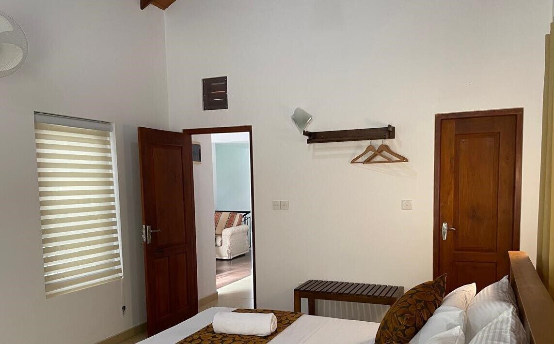 Une chambre à coucher comprenant un lit, une table de chevet, un porte-manteau suspendu et une porte donnant sur une autre pièce.