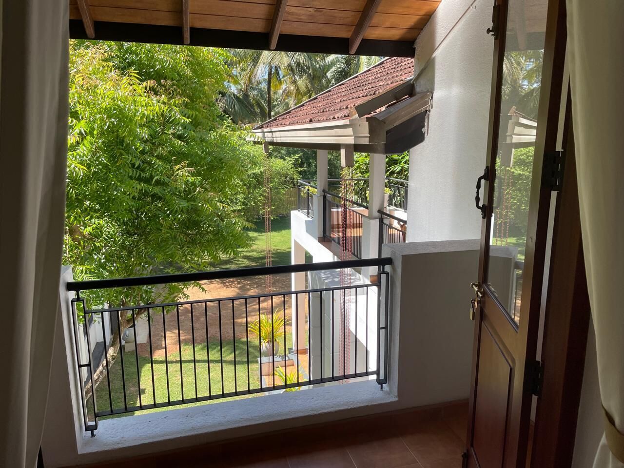 A balcony with a view of a garden and a building with a tiled roof.