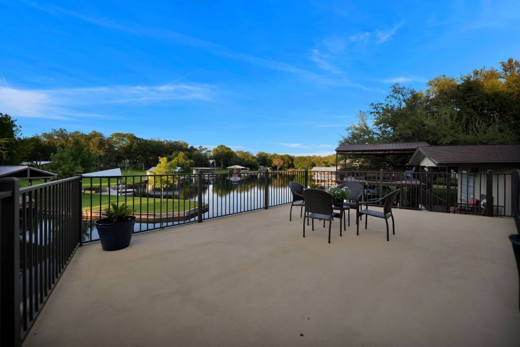 A covered patio with a view of a lake, a dining table with chairs, and a small garden area.